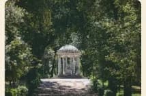 A garden pavilion at the end of a path through tall trees.